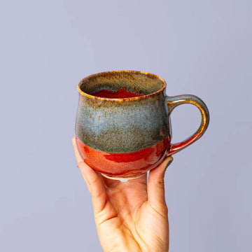 Hand holding a ceramic mug with a gradient design against a plain background.