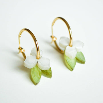 A pair of gold hoop earrings layered with a white flowers and green leaves through the hoop.
