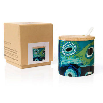 A sugar bowl printed with artwork by May Wokka with a wooden lid and a white spoon sticking out the side. There is a brown box next to the bowl.