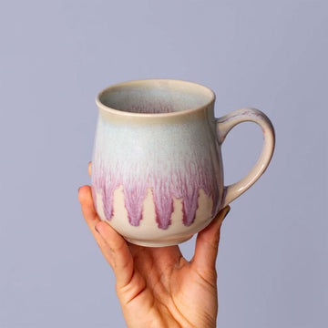 Hand holding a ceramic mug with a gradient design against a plain background.