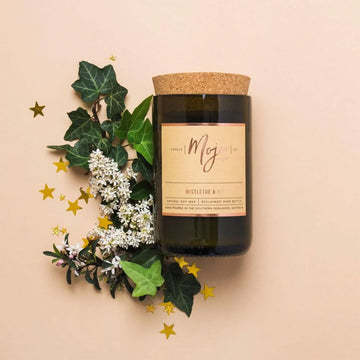 A candle made from a recycled wine bottle with the eading 'Mojo Mistletoe and Ivy' on the label next to mistletoe. 
