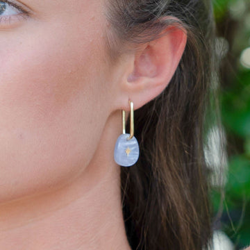 A pair of gold hoop earrings with a white coloured charm with a gold star hanging off the hoop.