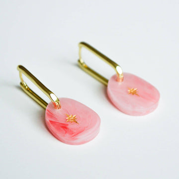 A pair of gold hoop earrings with an pink coloured charm with a gold star hanging off the hoop.