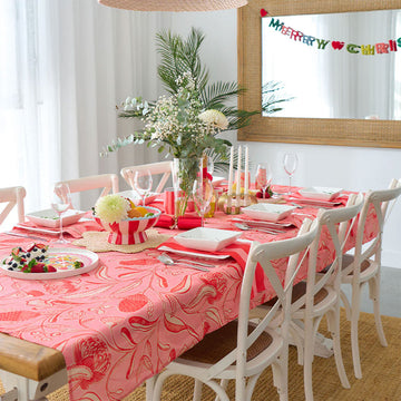 A folded up tablecloth printed with a red and pink floral pattern and a cardboard sleeve.