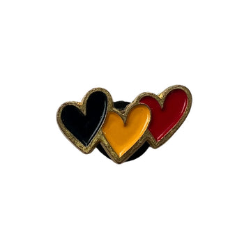 An enamel pin with three hearts, one in black, one yellow and one red, representing the Aboriginal flag.