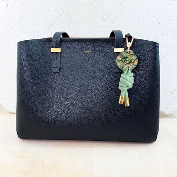 Keychain with green rope and leaf-patterned disc on a white background