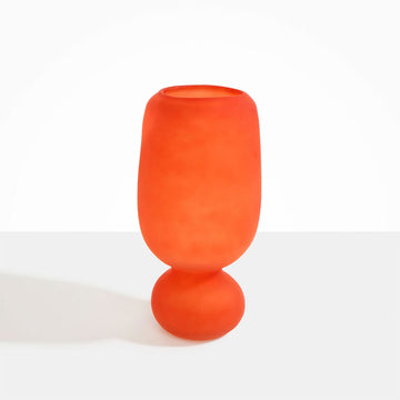 A tall frosted glass vase in orange with a sphere shaped bottom.