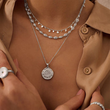 A rounded silver pendant with etchings on a silver chain necklace. 