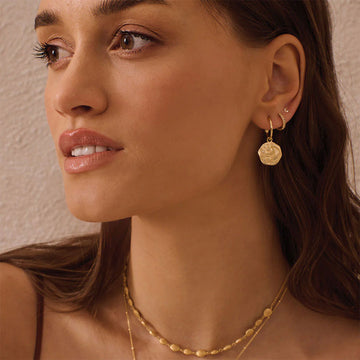 A pair of gold hoop earrings with a hexagon shaped pendant hanging off the hoop with an outline of a crescent moon.