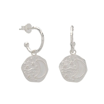 A pair of silver hoop earrings with hexagon shapes hanging off the hoop with an outline of a crescent moon.