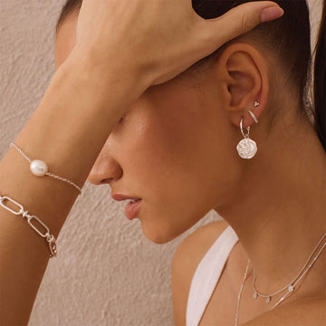 A pair of silver hoop earrings with hexagon shapes hanging off the hoop with an outline of a crescent moon.