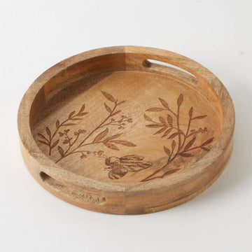 A small wooden round tray with cut out handles and an etched design of a bee and leaves.