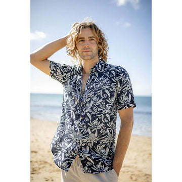 A model wears a short sleeve blue and white shirt with beige pants while standing at the beach.
