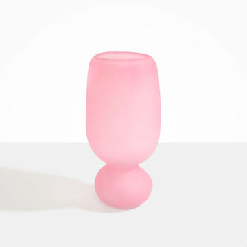 A tall frosted glass vase in pink with a sphere shaped bottom.