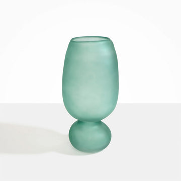 A tall frosted glass vase in teal with a sphere shaped bottom.