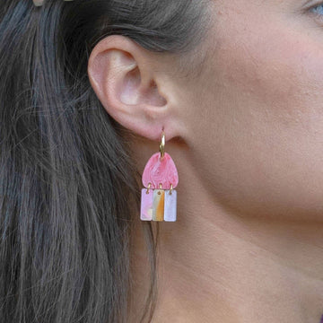 A pair of gold hoop earrings with pink coloured charms hanging off the hoop.