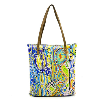 A tote bag with brown straps and printed with artwork by Judy Watson.