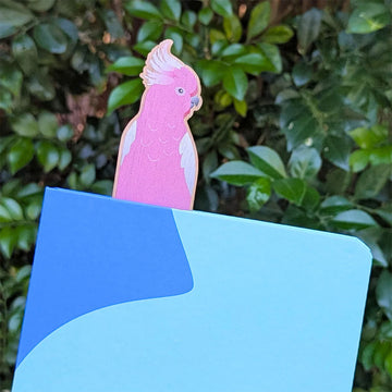 Pink wooden bookmark shaped like a galah bird attached to packaging on a white background.