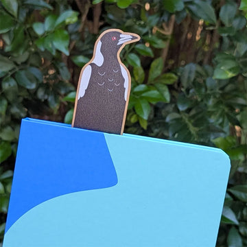 Wooden bookmark with magpie design attached to packaging on a white background.