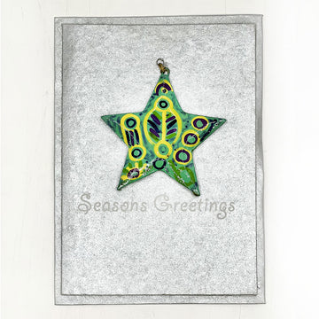 A silver card with the text 'Seasons Greetings' written on it and a star shaped ornament printed with artwork by Cedric Varcoe.