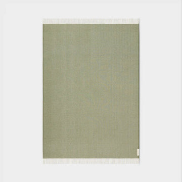 Green throw with white border on a white background.