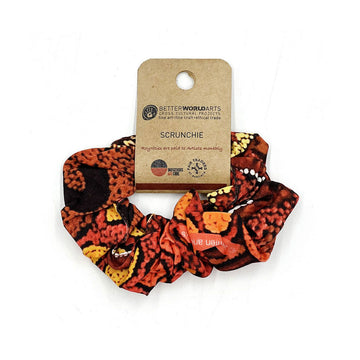 A scrunchie printed with artwork in shades of orange and brown attached to a brown card.