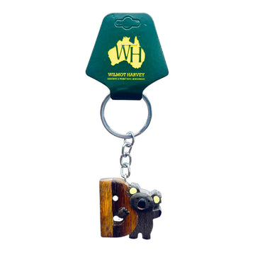 Keychain with koala design and wooden texture, attached to a green packaging with 'WH' logo.