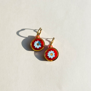 A pair of round earrings with a white flower in the middle attached to gold hoops.
