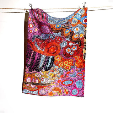 A cotton tea towel printed with artwork by Andrea Mimpitja Adamson is hanging off a thin rope.