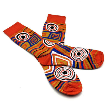A pair of socks in orange printed with artwork by Mary Napangardi Brown are overlapping each other.
