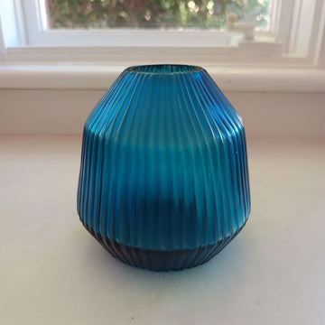 Blue ribbed glass vase on a white surface with a window in the background.