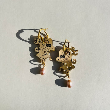 A pair of gold octopus earrings with an orange pearl attached at the bottom attached to a gold hoop.