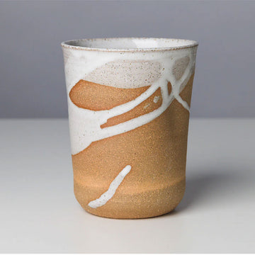 A ceramic mug in a natural colour with white paint over the top in an uneven application.