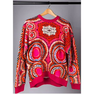 A jumper printed with artwork by Murdie Morris in shades of pink and red attached to a coat hanger.