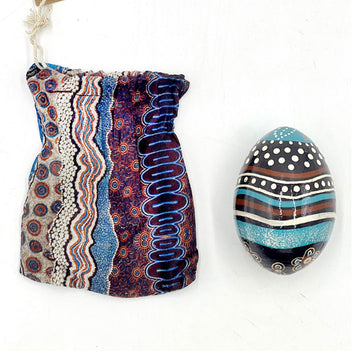An ornamental egg printed with artwork by Bianca Gardiner-Dodd next to a matching fabric sleeve.