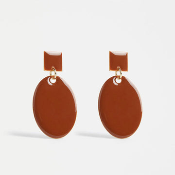 An image of a pair of earrings in a glossy enamel Spice coloured finish with a large oval drop from a smaller square stud.