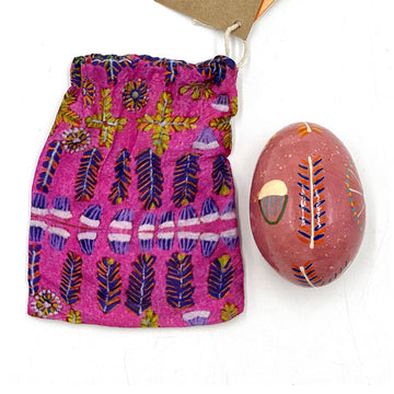An ornamental egg printed with artwork by Rosie Ross next to a matching fabric sleeve.
