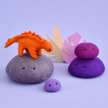 An orange stegosaurus made from felt standing on a grey felt rock. There are purple felt rocks surrounding.
