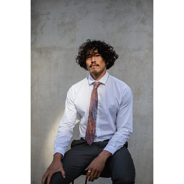 A tie featuring artwork by Minyawe Miller in black, yellow and orange.