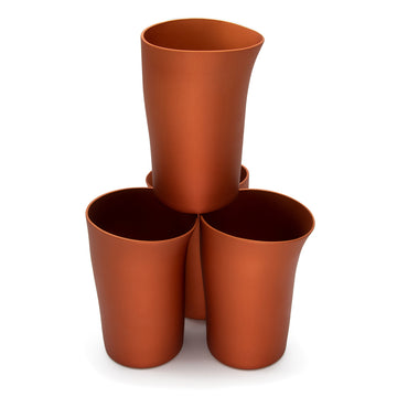A set of four beakers in copper with a handcrafted shape are stacked up next to each other. One beaker is on top of the other three.