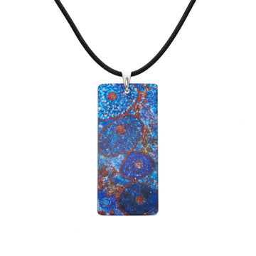 A rectangle pendant printed with artwork by Alma Granites in blue on a black cord.