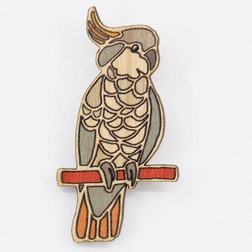 A wooden Australian cockatoo bird brooch sitting on a pirch. 
