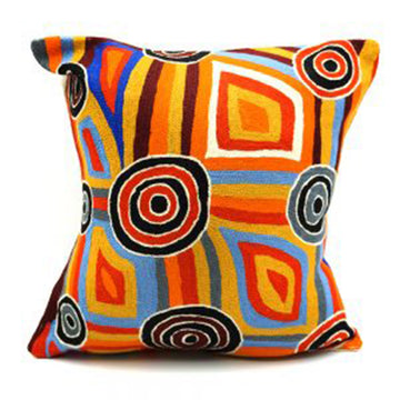A cushion featuring a circle and square design in orange, black, grey and red with artwork by Mary Napangardi Brown.