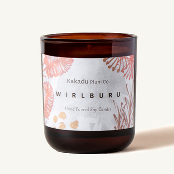 Candle by Kakadu Plum Co. Wirlburu. Presented in a dark amber votive with pink blossoms on a white label.