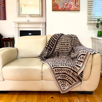 A throw blanket is draped over a couch. The throw has black and white artwork by Cynthia Burke.