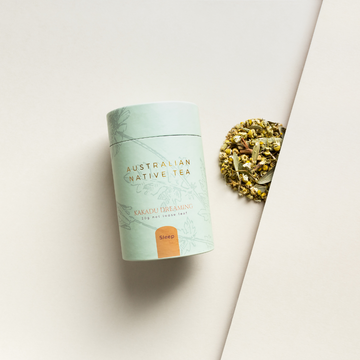Kakadu Tea. Packaged in a light green canister with gold and orange text next to some loose leaf tea.