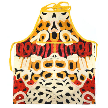 An apron is laid out flat featuring artwork in red, yellow and cream by Anmanari Brown.