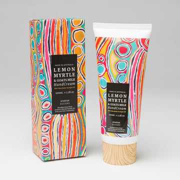 A tube of hand cream with a wooden look lid and box packaging. The box and tube feature artwork by Judy Watson in red, green, orange and blue.