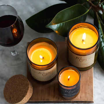 A candle made from a wine bottle with a cork lid is laying down surrouned by cherries, chocolate and pomegrantes.