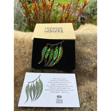 Enamel on metal brooch depicting a group of colourful green gum leaves with yeallow highlights.  